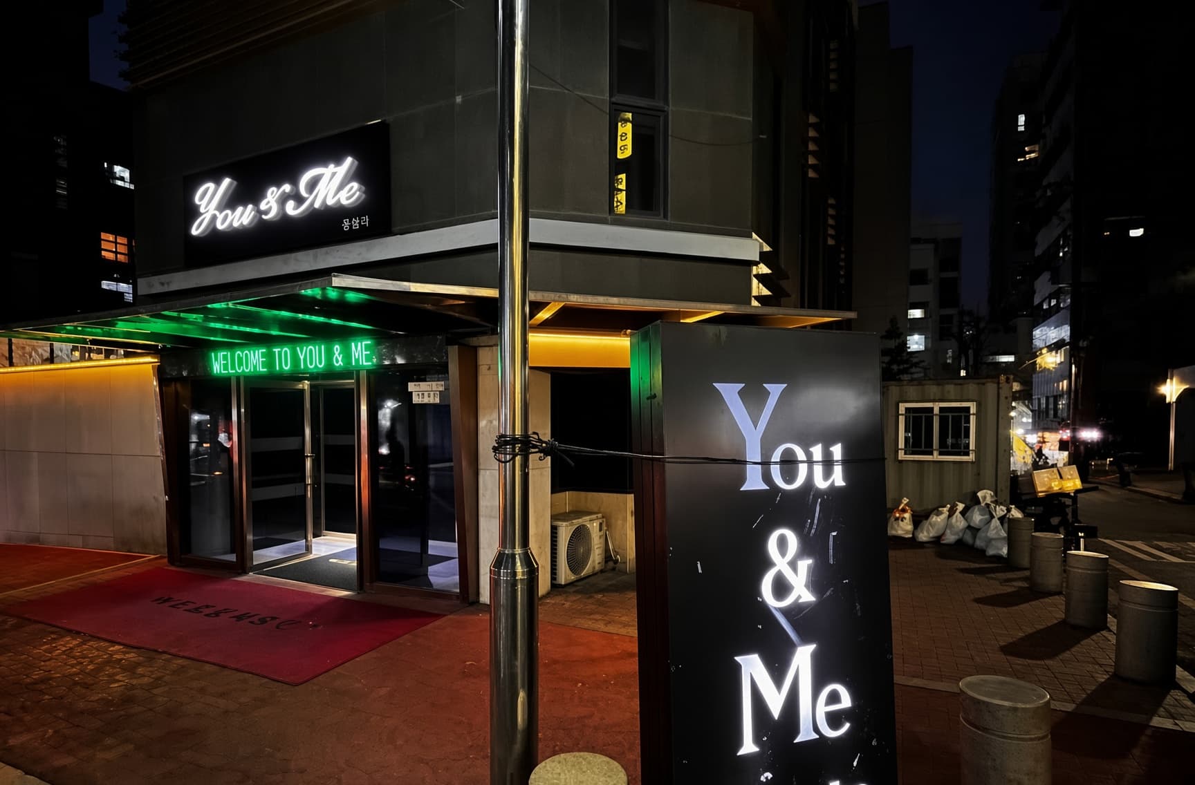 カンナム・ユーアンドミー (강남 유앤미) · You & Meの看板と緑の照明、赤い入口の床が見えます。