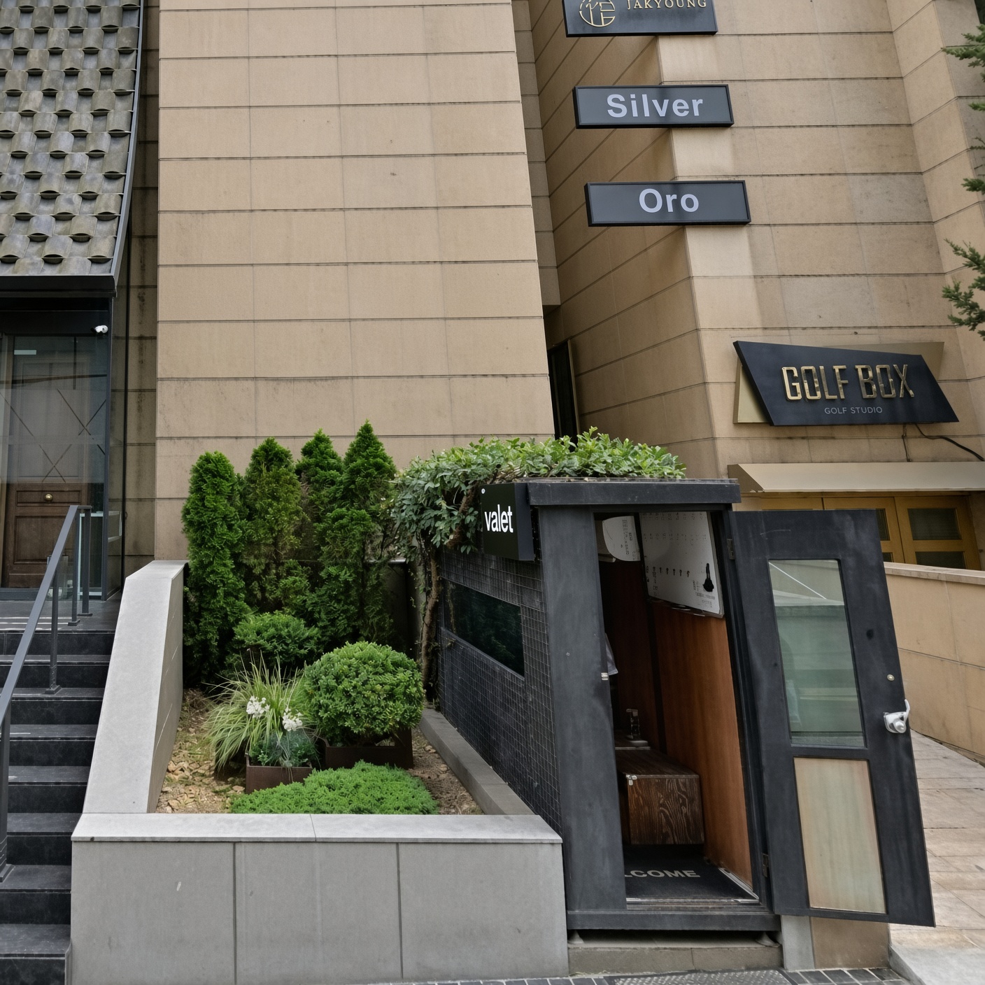 강남 모짜르트 · 건물 앞 화단과 어두운 출입구, 위쪽의 여러 안내 간판이 보입니다.